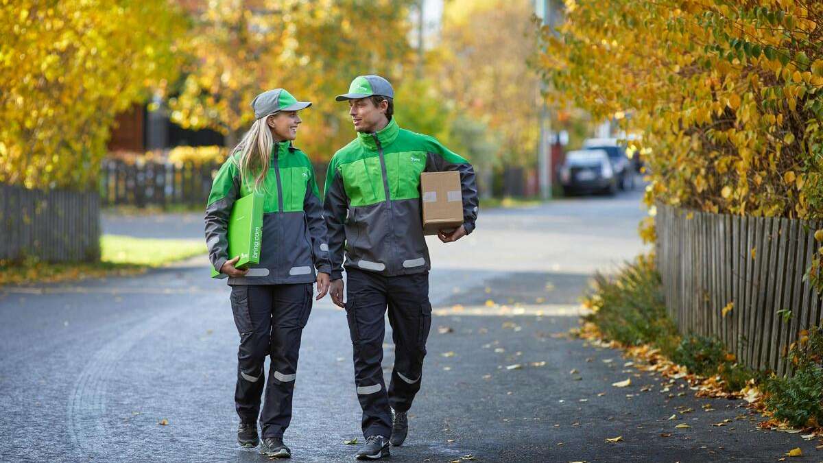 Two couriers in Bring uniform, they each have a parcel under their arm.