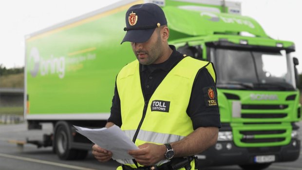 Customs officer checks documents in front of a green delivery van.