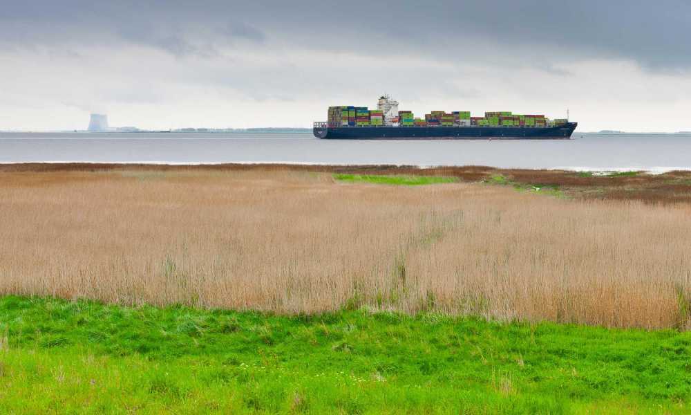 A blue cargo ship loaded with mostly green containers