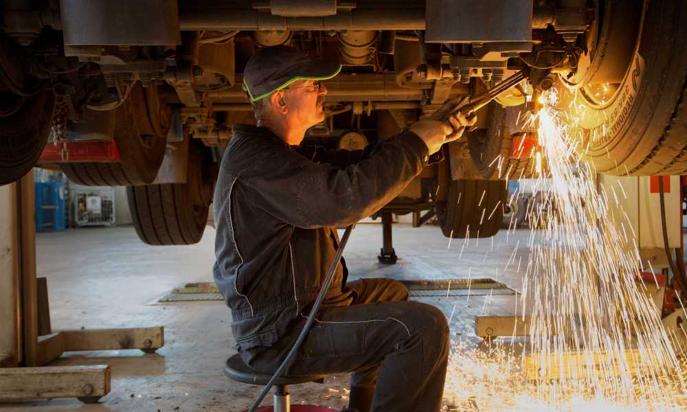 A man is repairing something under a car in a garage.