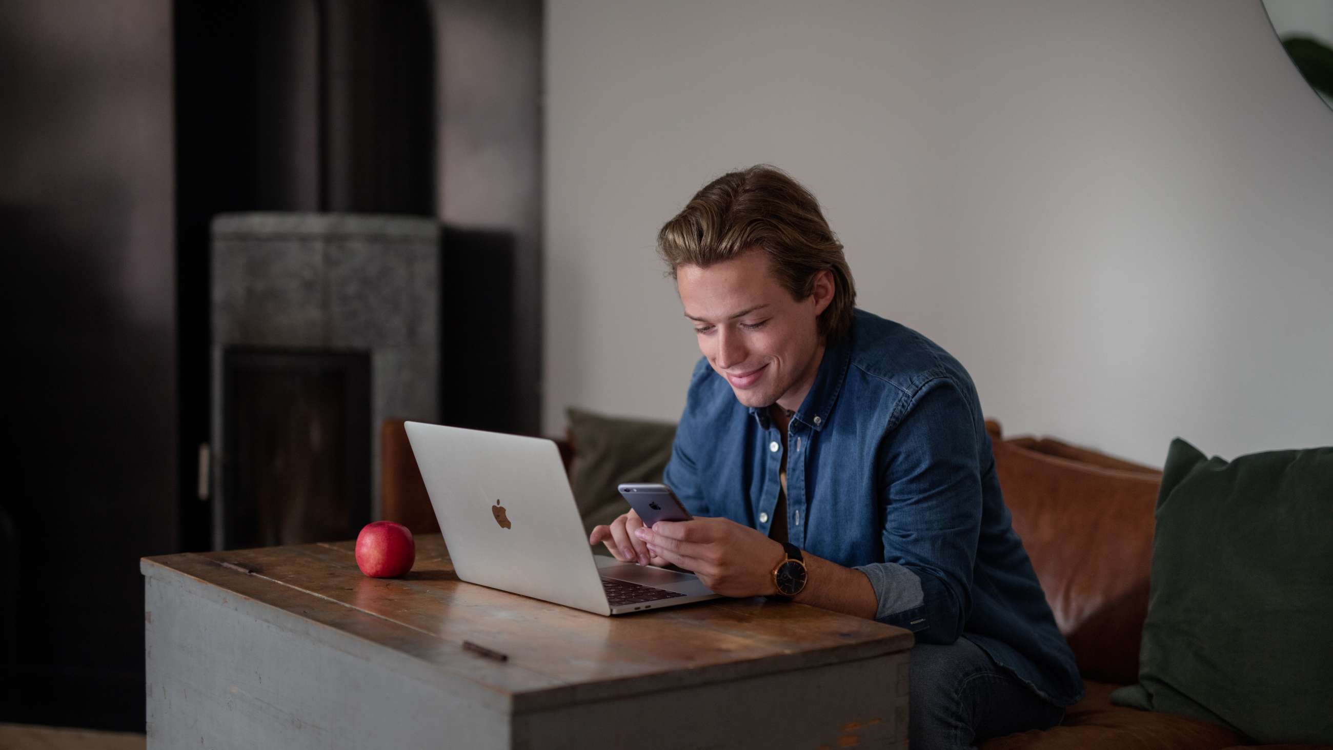En ung mann som sitter foran en laptop og holder en iPhone i hånda