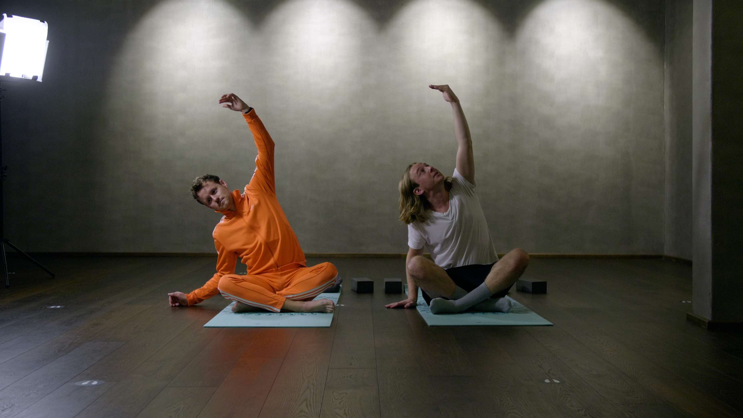 Sebastian Rasch og Mads Krogh som sitter på yogamatter på gulvet med armene opp i været
