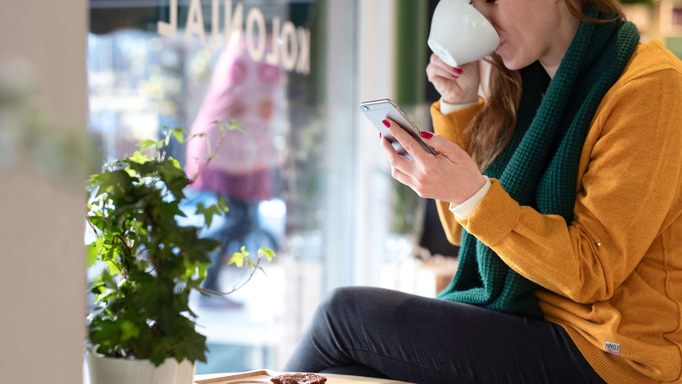 En kvinne som ser på mobilen samtidig som hun drikker kaffe