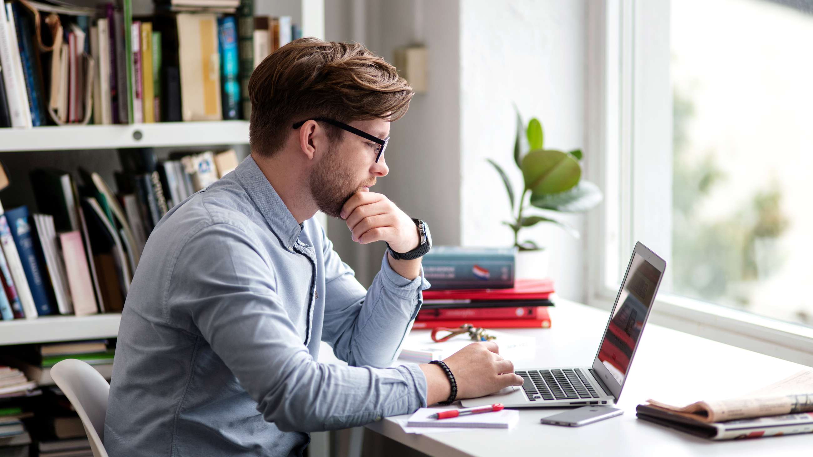 Man sitter foran vindu med sin laptop.