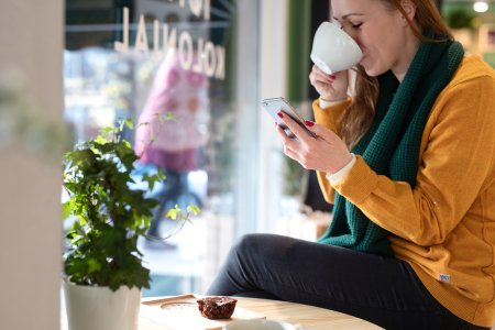 En kvinne som ser på mobilen samtidig som hun drikker kaffe