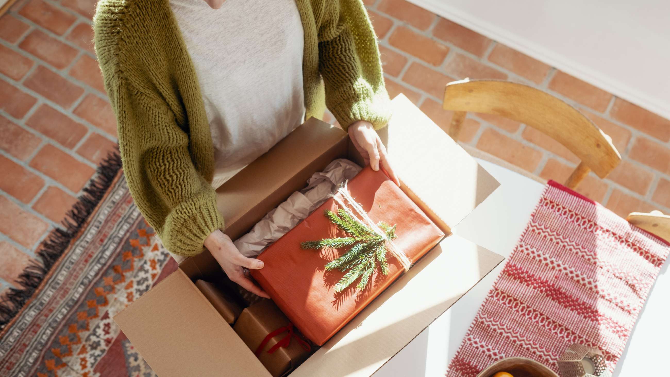 En kvinne legger en julegave i en pakke.