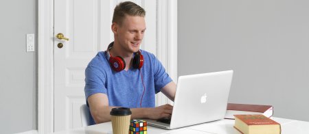 En mann med røde hodetelefoner rundt halsen som ser på en laptop