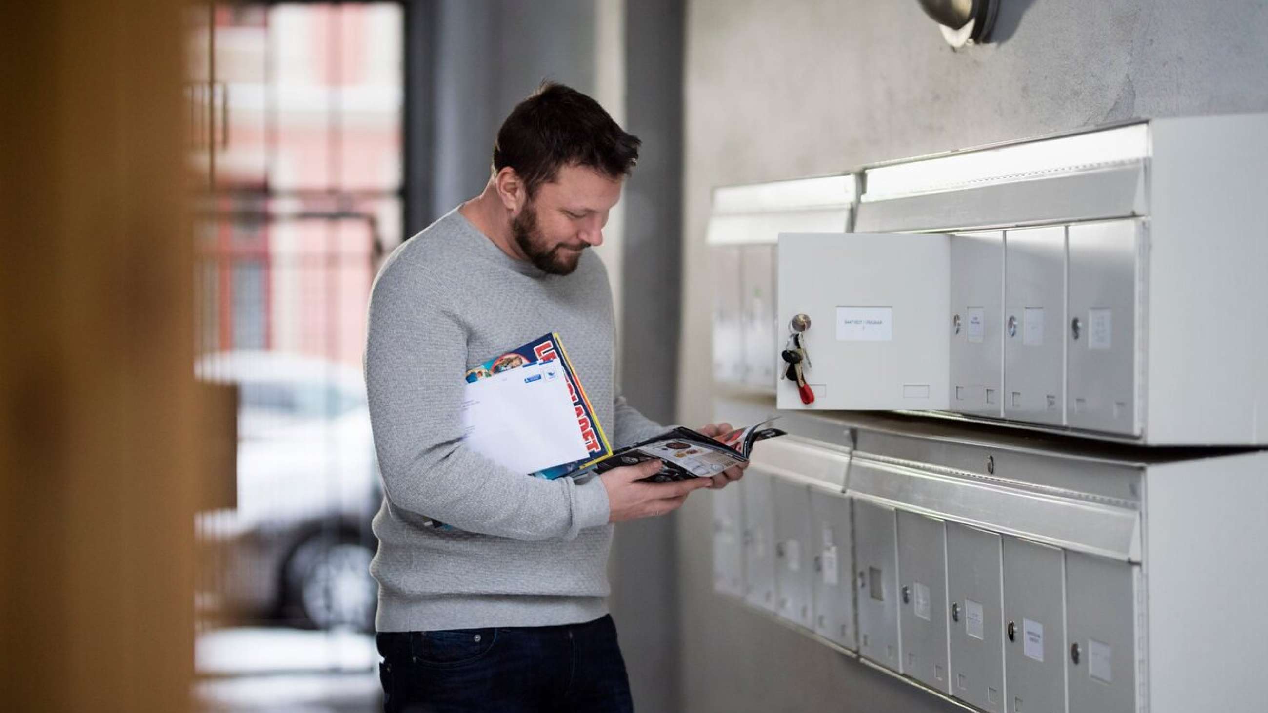 En mann som leser i en reklameavis ved siden av en åpnet postkasse