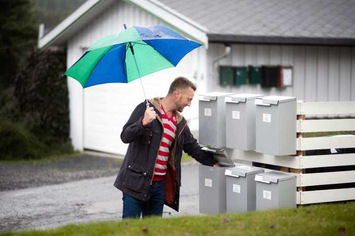 En mann med paraply som står foran postkasser