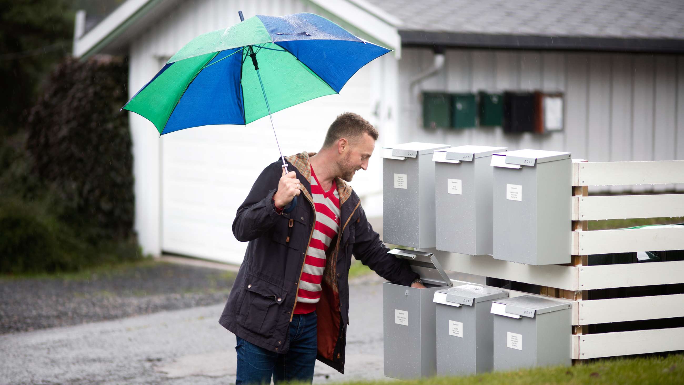 En mann med paraply som står foran postkasser