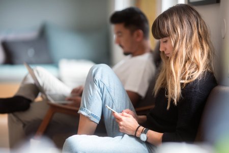 Et ungt par sitter i sofa med sine digitale enheter, pc og mobil.
