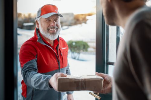 En Bringbud står i en døråpning og leverer en pakke hjem til noen