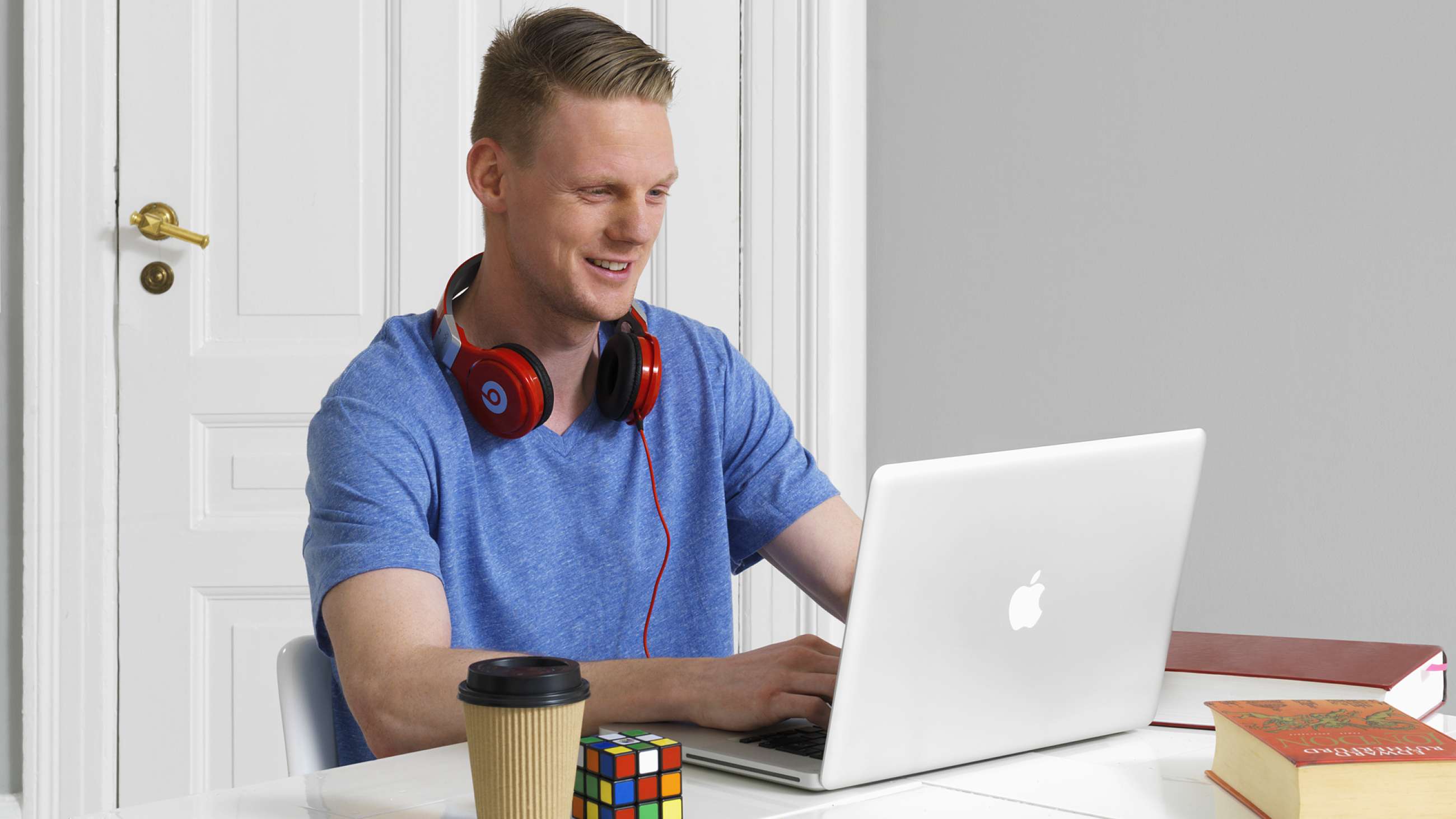 En mann med røde hodetelefoner rundt halsen som ser på en laptop