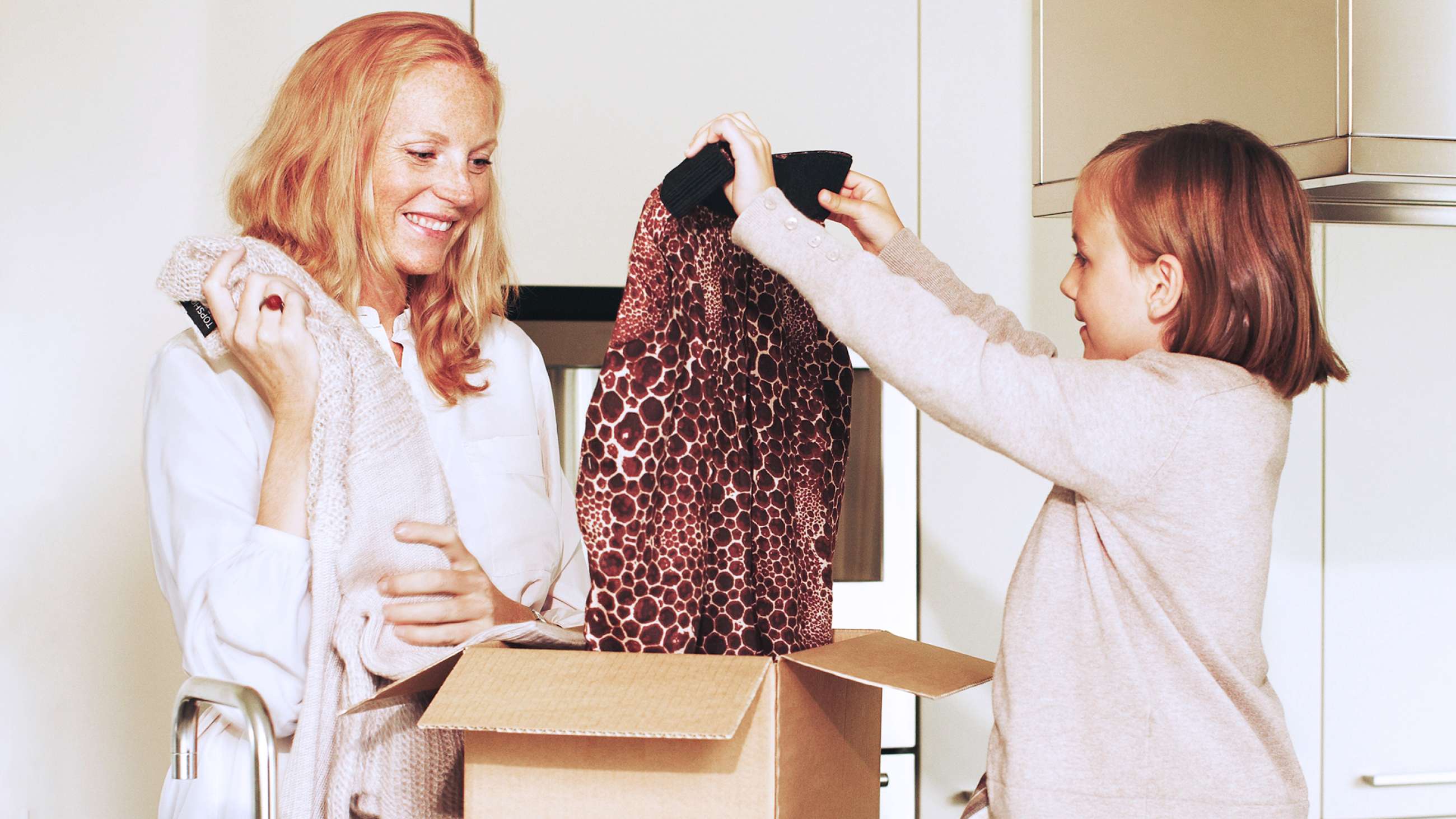 En kvinne og et barn som pakker ut klær fra en pappeske.
