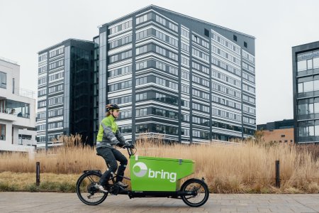 Bringbud på grønn elsykkel transporterer pakker i et boligområde.