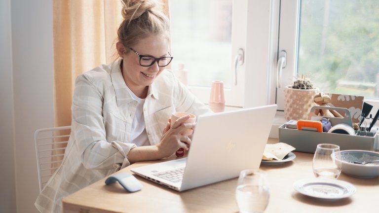 Smilende kvinne sitter foran sin laptop