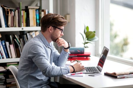 Man sitter foran vindu med sin laptop.