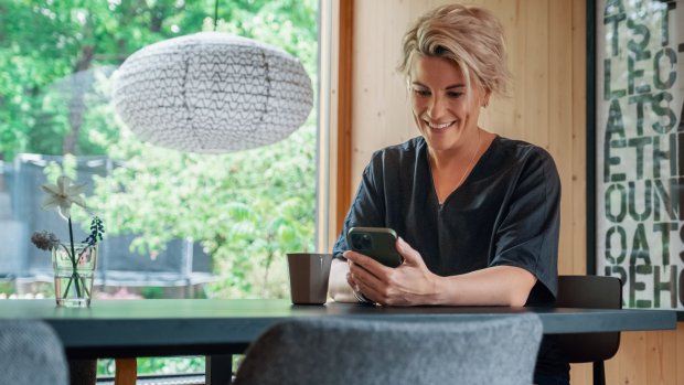 Kvinne sitter ved et bord og sjekker sin mobil