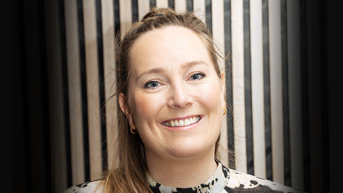 Nærbilde av Walle-Hansen i blomstrete bluse foran en trevegg.