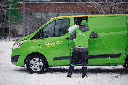 Bring-sjåfør tar ut pakker fra varebil. Vinterbilde.