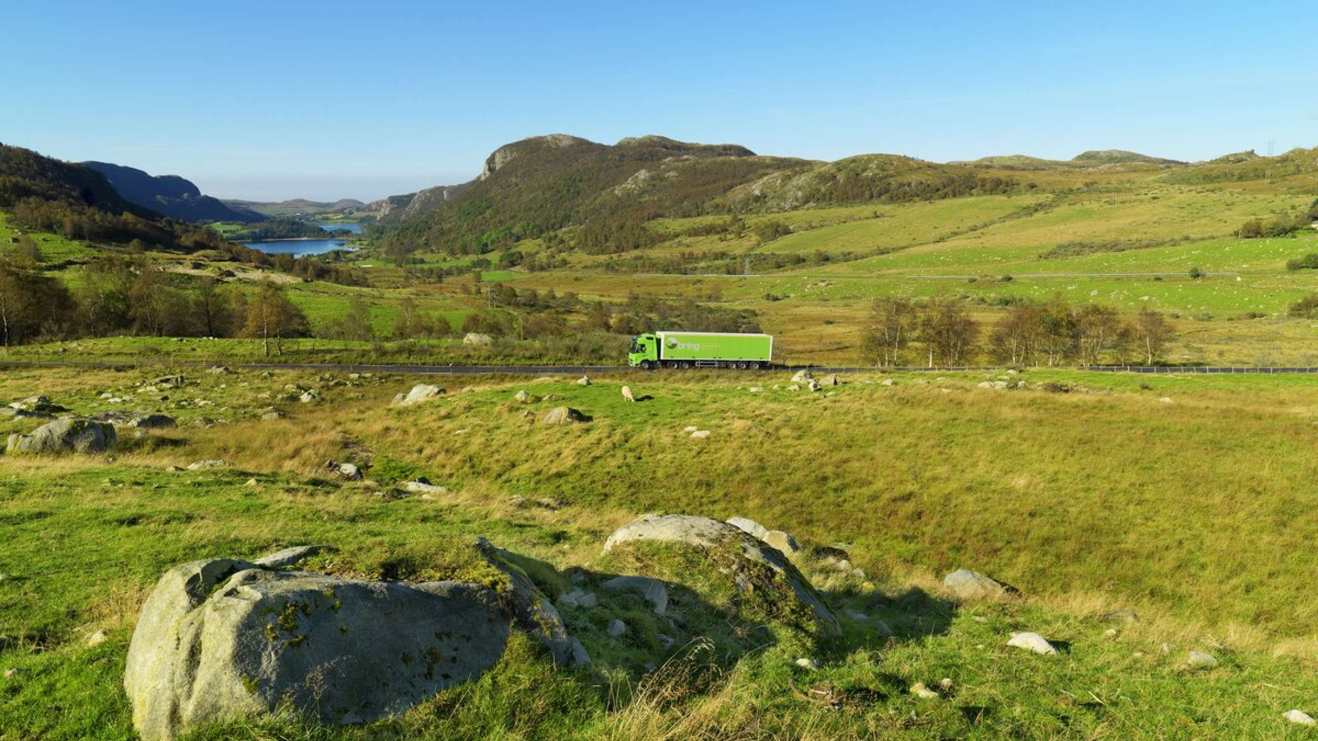 En Bring-lastebil kjører på en vei i et grønt landskap.
