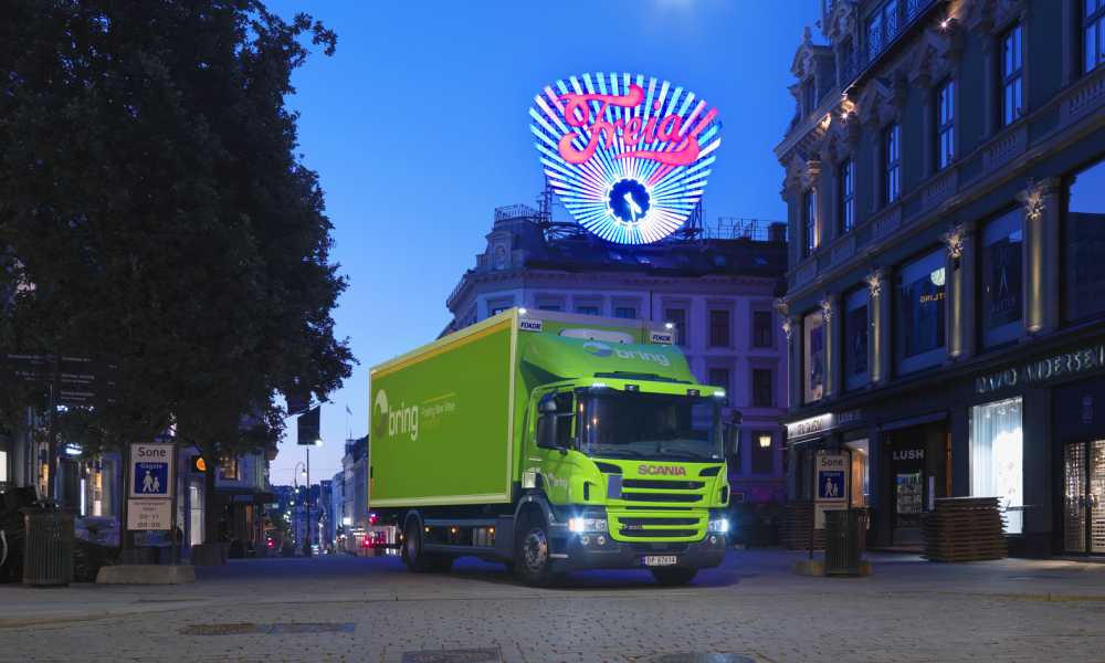 Grønn bring-lastebil kjører nedover Karl Johan en grytidlig morgen.
