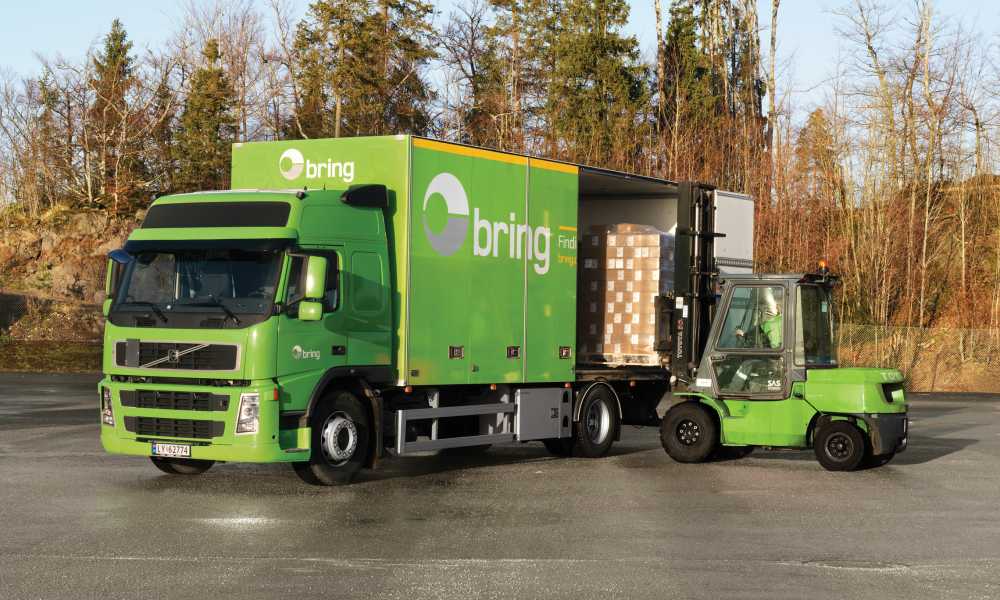 Grønn truck laster paller fra siden inn på en Bring lastebil.