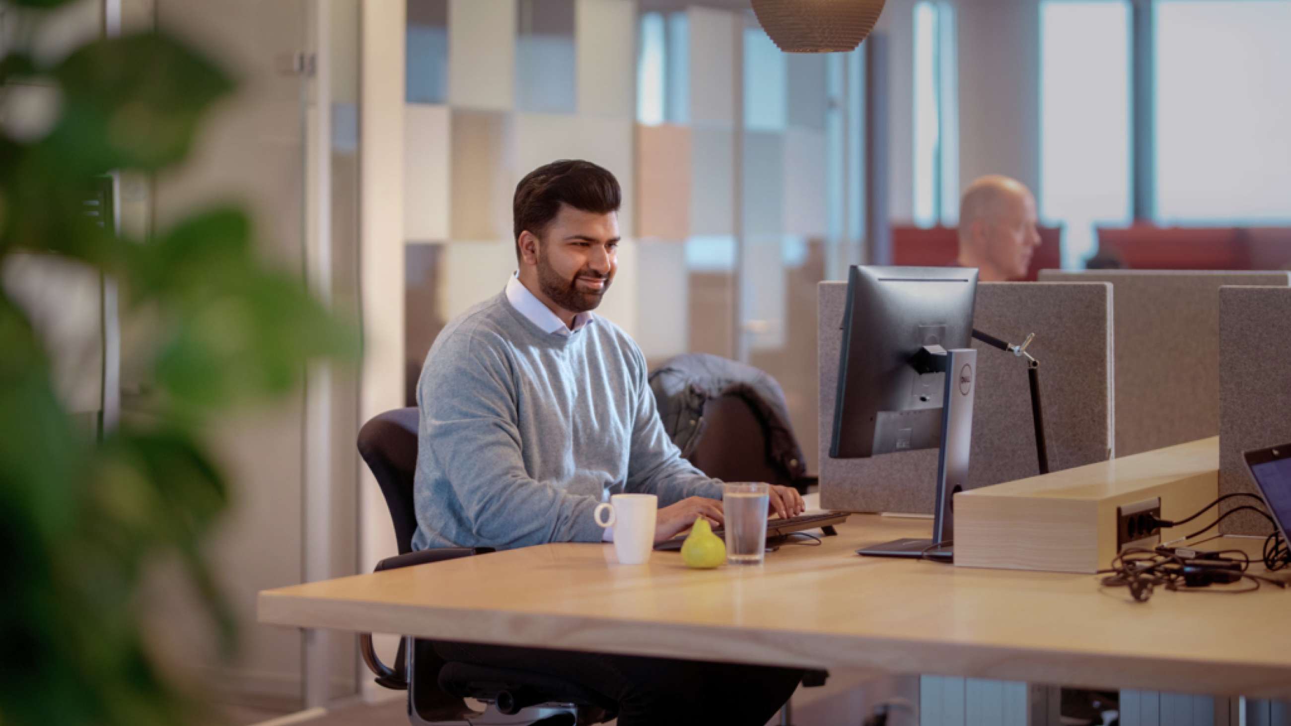 Mann sitter foran PC på kontor med glassvegger bak seg.