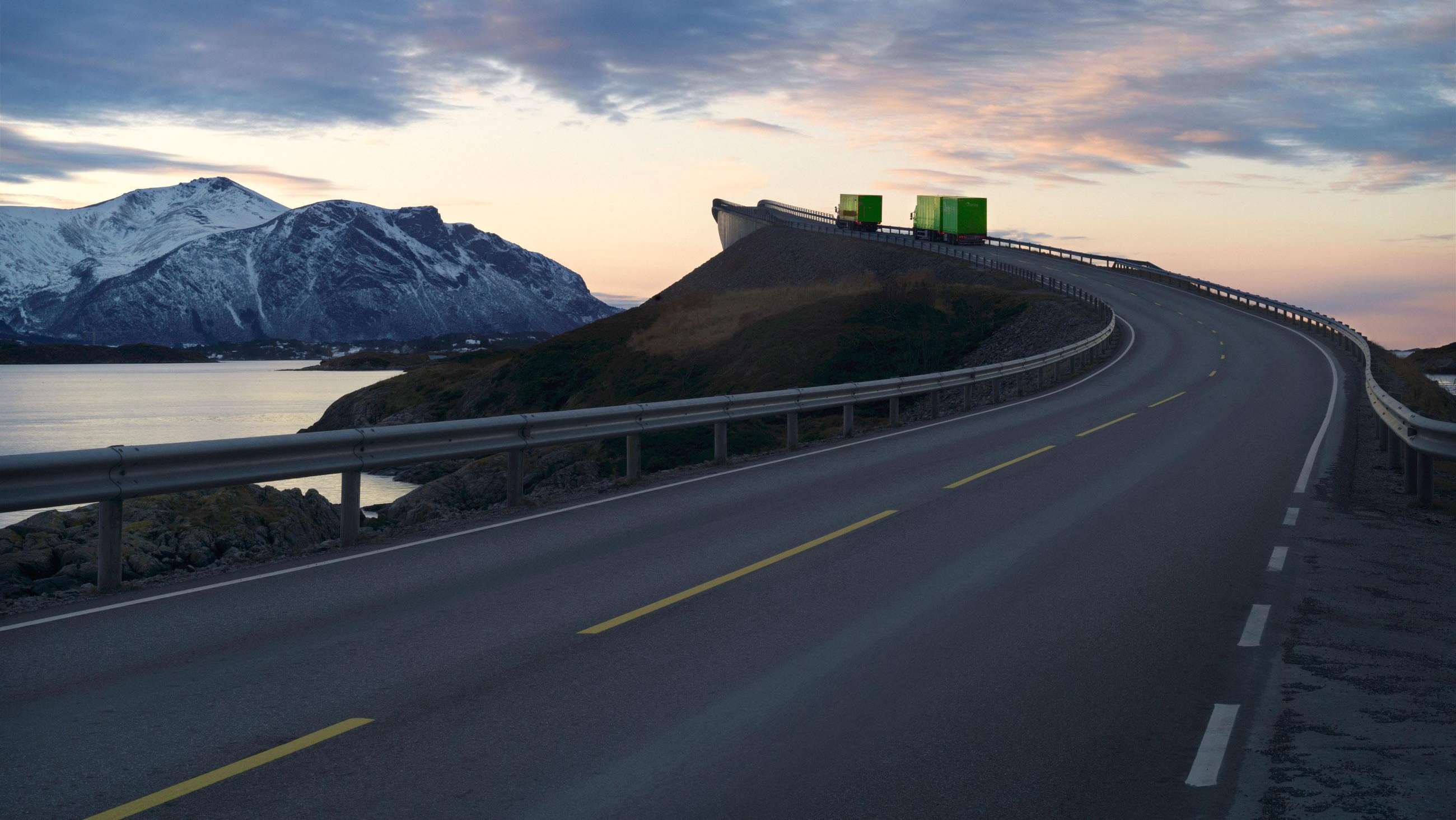 To grønne lastebilder kjører over en lang bro.