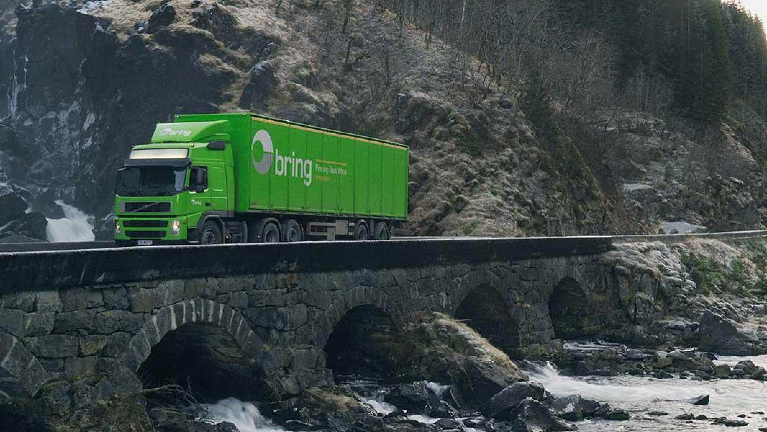 Grønn lastebil fra Bring kjører over steinbru.